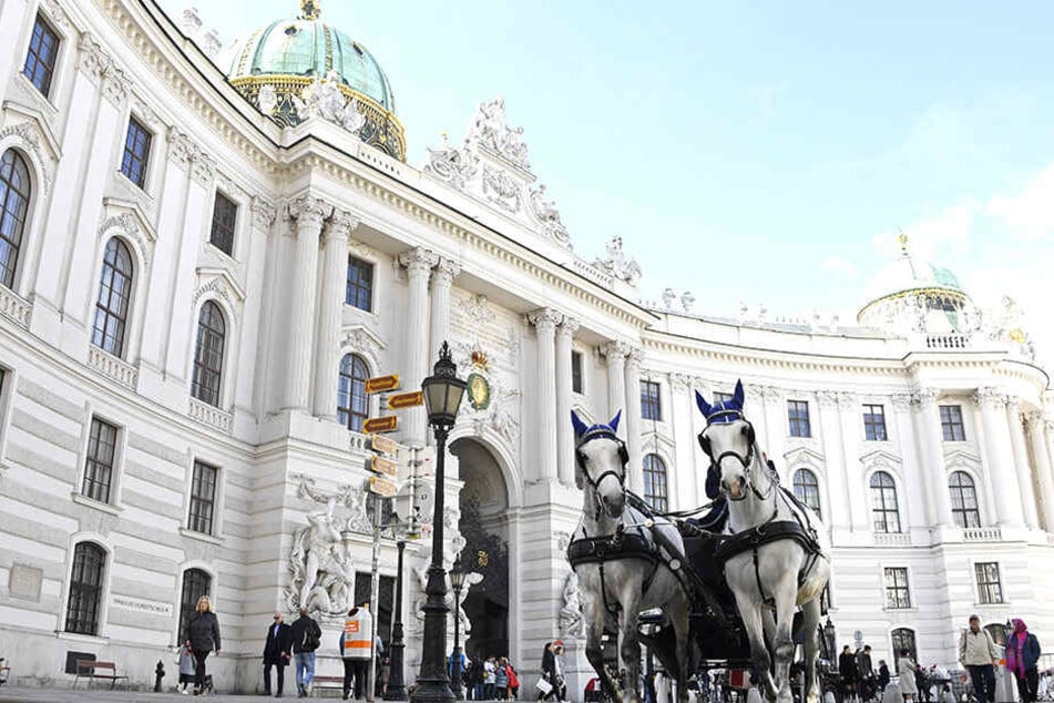ine Pferdekutsche fährt am Michaelerplatz vor der Wiener Hofburg entlang.