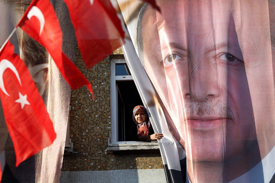 Die Türkei vor den Wahlen: Eine Frau blickt in Istanbul aus ihrem Fenster hinter einem Banner des türkischen Präsidenten Erdogan hervor.