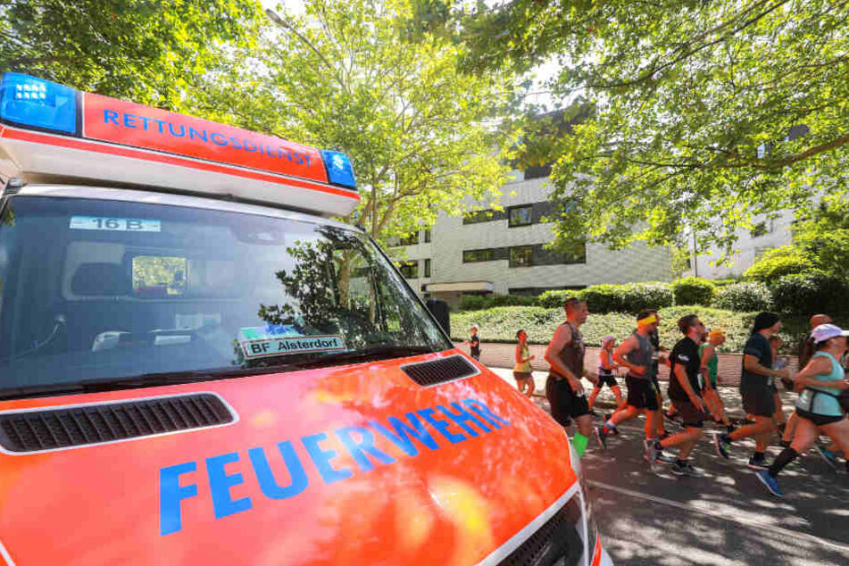 Ein Rettungswagen steht am Straßenrand der Strecke, während die Läufer passieren.