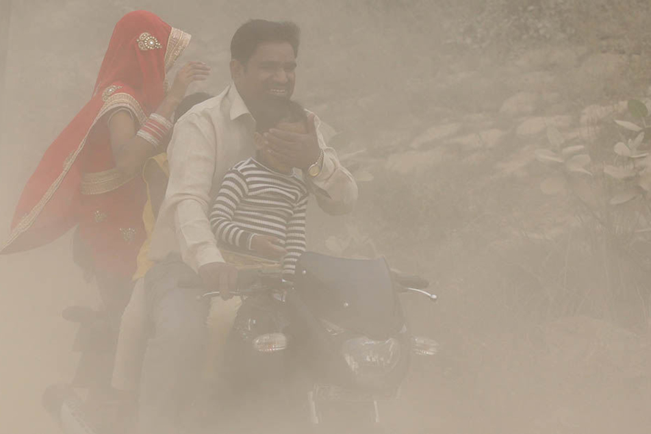 Ein Mann fährt in Neu Delhi seine Familie auf einem Motorroller durch dichten Smog- Nebel und hält seinem Sohn die Augen zu.