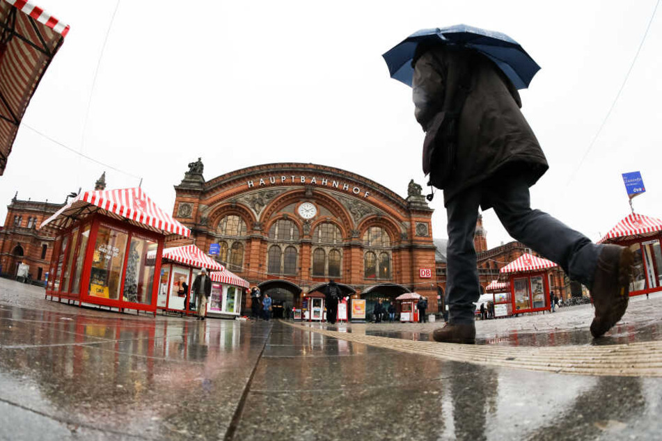 Ein Mann geht bei regnerischem Wetter mit einem Regenschirm in Richtung Hauptbahnhof Bremen.