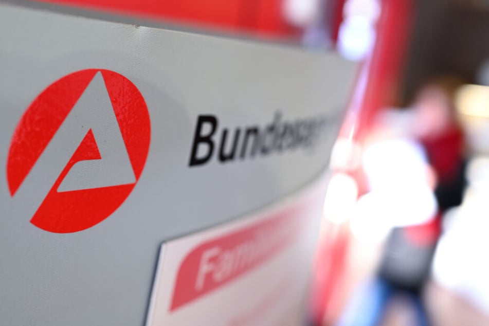 Ravensburg: Auf einer Stele ist das Logo der "Bundesagentur für Arbeit" zu sehen, während im Hintergrund ein Besucher am Informationsschalter steht. (Symbolbild)