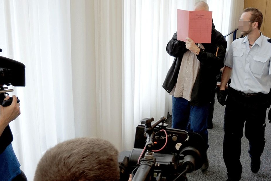 Der Angeklagte in einem Prozess um die Tötung seines Sohnes mit Kohlenmonoxid verdeckt am 21. Juni beim Betreten des Gerichtssaals sein Gesicht mit einem Aktenordner.