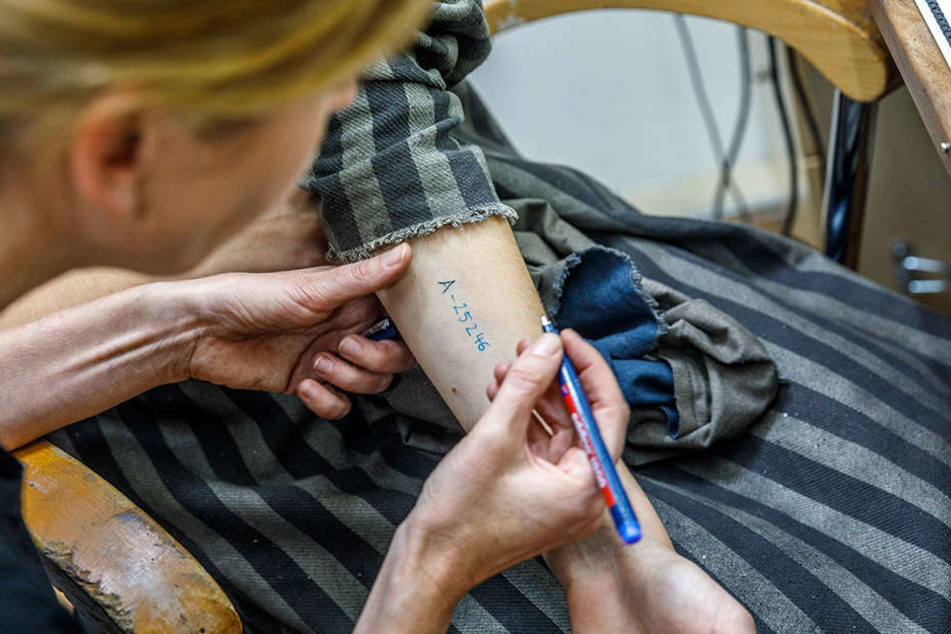 Mit einem haltbaren Stift schreibt die Maskenbildnerin den Schauspielern die
KZ-Nummer auf den Unterarm.
