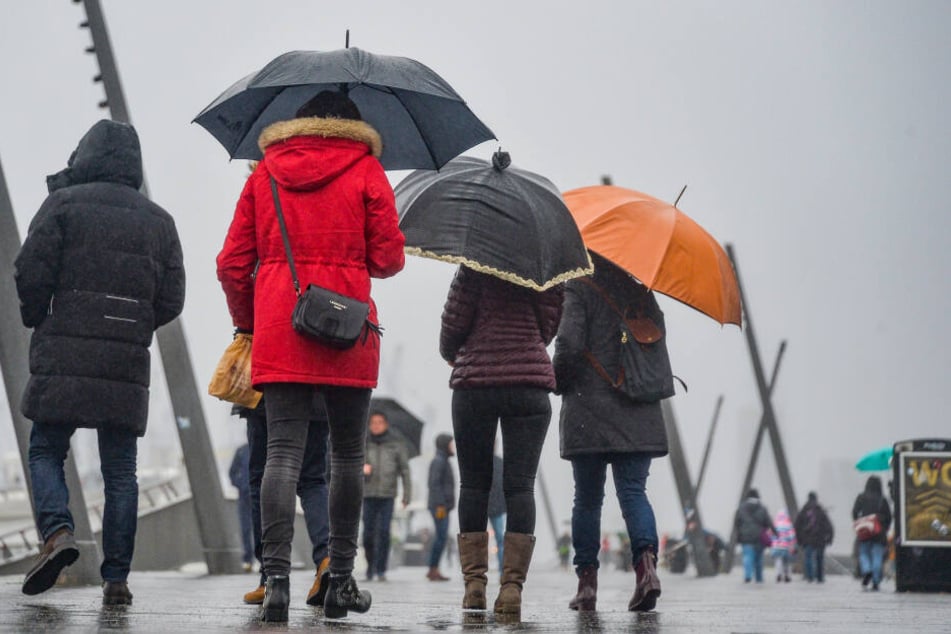 Passanten gehen bei Regen und Kälte über die Landungsbrücken am Hamburger Hafen.