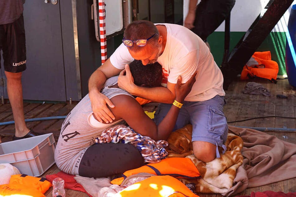 Ein Besatzungsmitglied des spanischen Rettungsschiffes "Open Arms" tröstet einen Migranten. Die dramatische Lage auf dem spanischen Rettungsschiff ist eskaliert.