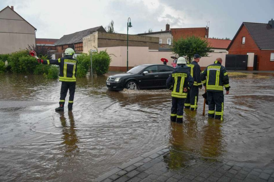Feuerwehrmänner stehen nach Starkregen auf einer überfluteten Straße im Landkreis Börde.