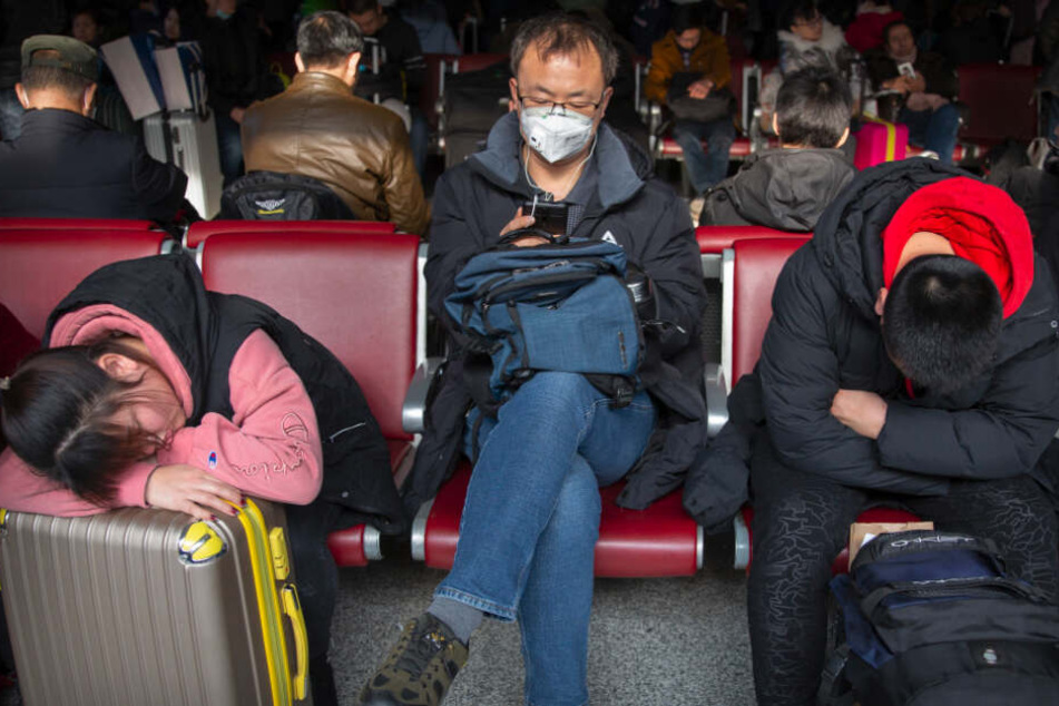 Reisende tragen als Schutzmaßnahme gegen die Verbreitung des Corona-Virus Mundschutz, während sie in einem Wartezimmer am Pekinger Westbahnhof sitzen.