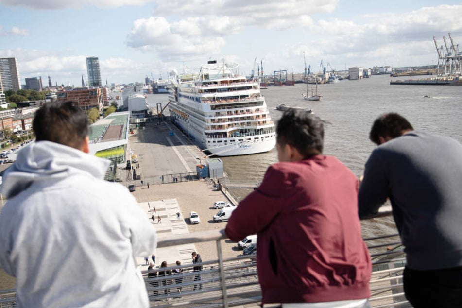 Drei Männer schauen auf das Kreuzfahrtschiff "Aida Sol" am Cruise Center Altona.