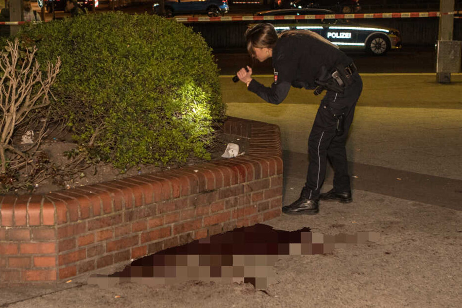 Eine Polizistin sucht mit einer Taschenlampe ein Gebüsch nach Spuren ab.