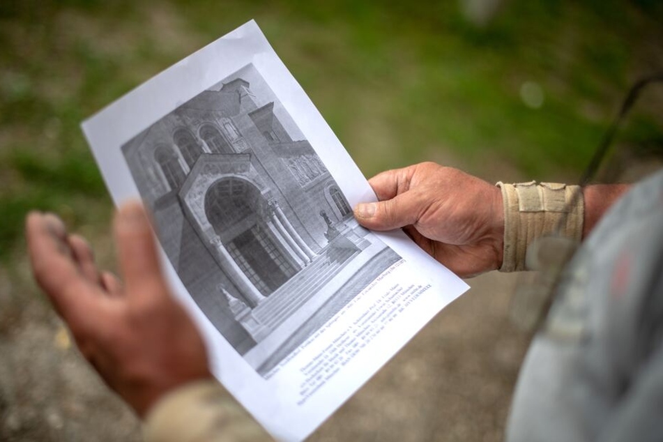 Vor der Sphingen-Bauhütte am Friedhof zeigt der Steinmetzmeister Wolfgang Gottschalk ein altes Foto, das die verschwundenen Sphinx-Figuren vor dem Eingangsportal des Münchner Nordfriedhofs zeigt.