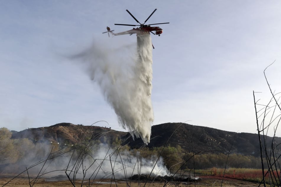 Ein Löschhubschrauber wirft in Fallbrook, Kalifornien, USA, seine Wasserladung über einem Schwelbrand von Holzschnitzeln und Mulch ab.