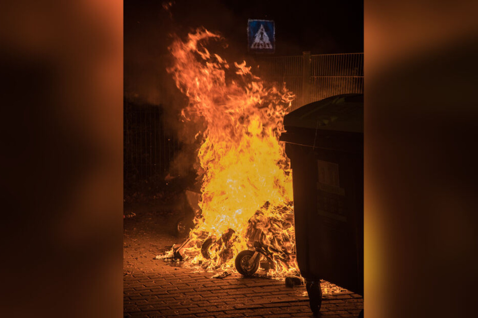 Flammen schlagen aus der bereits völlig in sich zusammen geschmolzenen Mülltonne.