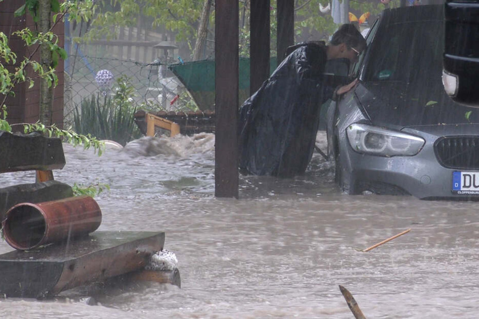In Plaue steht ein Mann im vom Wasser überfluteten Garten neben einem Auto.