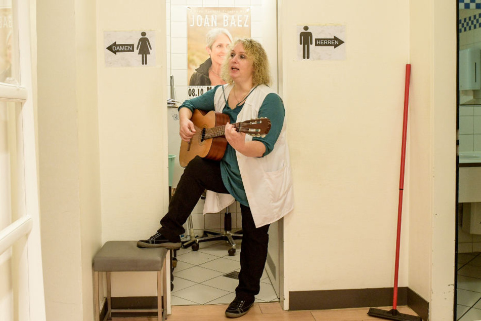 Stefanie Ansul-Weissner steht mit ihrer Gitarre zwischen den Toiletten und singt.