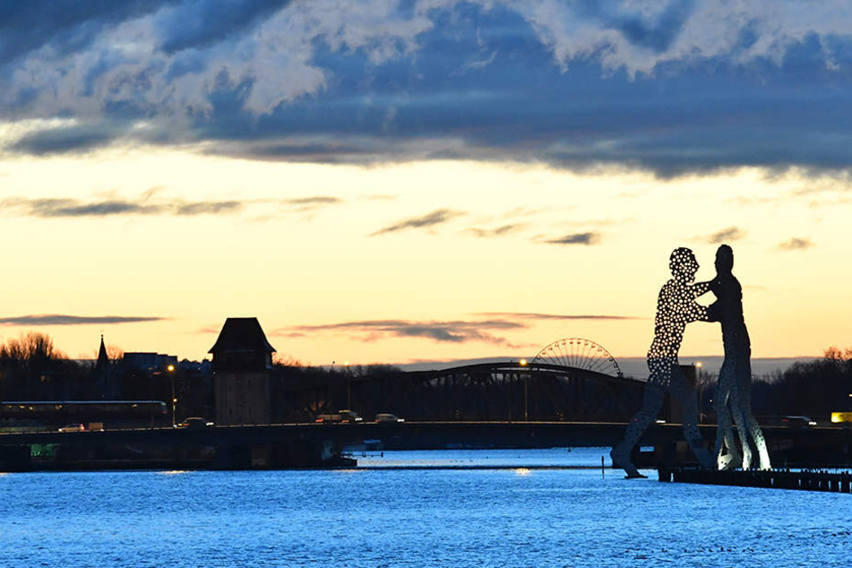 Farbenfroh zeigt sich in Berlin der Himmel über der Elsenbrücke und der Skulptur Molecule Man.