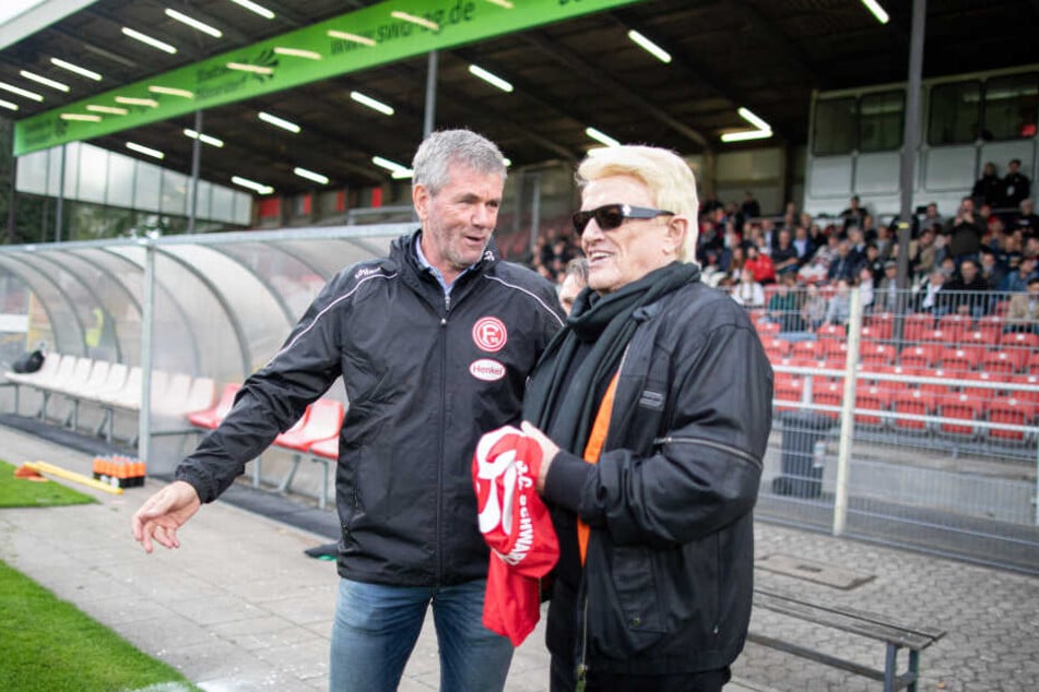 Heino (80) steht vor den Anstoß für das Benefizspiel auf dem Spielfeld neben Fortuna Trainer Friedhelm Funkel (65).