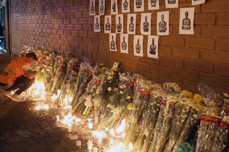 Die Bilder der Spieler an einer Wand, darunter viele Blumen und Kerzen.
