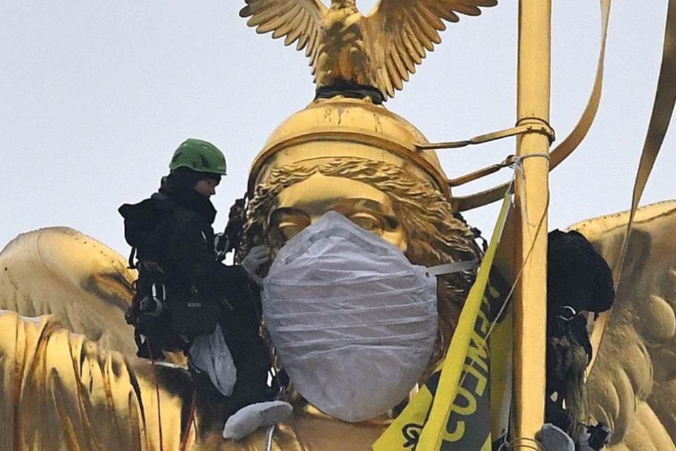 Greenpeace-Aktivisten schnallen dem Mundschutz an der Viktoria fest.
