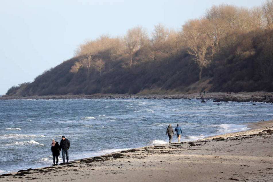 Spaziergänger laufen an einem Ostsee-Strand entlang. (Symbolbild)