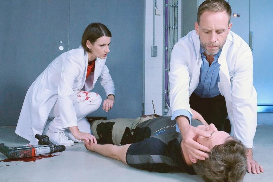 Hausmeister Henrik Weitzmann hat sich den Akkubohrer in die Leiste gerammt. Maria Weber und Kai Hoffmann eilen zu ihm.