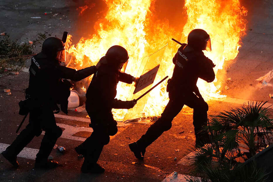 Polizisten laufen am Freitagabend an einer brennenden Straßenbarrikade in Barcelona vorbei.