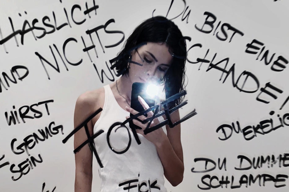 Die Sängerin Lena Meyer-Landrut fotografiert vor einem Spiegel, auf dem diverse Beschimpfungen stehen, die sie erreicht haben, ein Selfie.