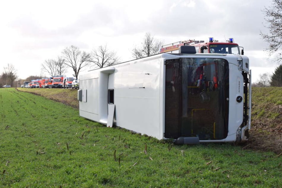 Der verunfallte Schulbus liegt umgekippt neben der Fahrbahn einer Landstraße.