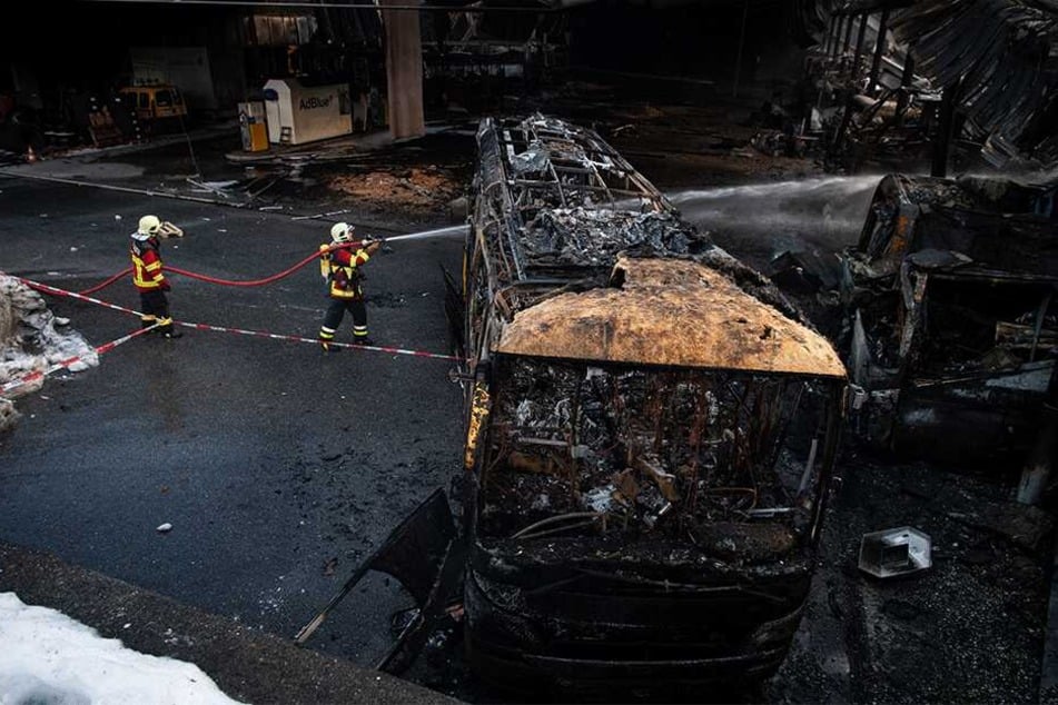 Feuerwehrleute löschen einen ausgebrannten Bus in dem Busdepot.
