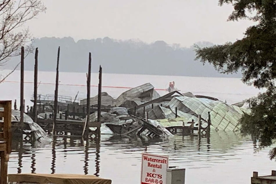 Ein Dock und viele Boote liegen nach einem Feuer zerstört im Wasser.