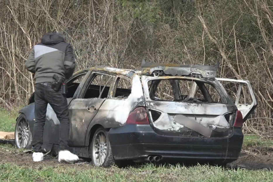 Ein Polizeibeamter neben dem ausgebrannten Fluchtauto in Köln. Beim Überfall in Limburg waren die Täter ähnlich vorgegangen (Archivbild).