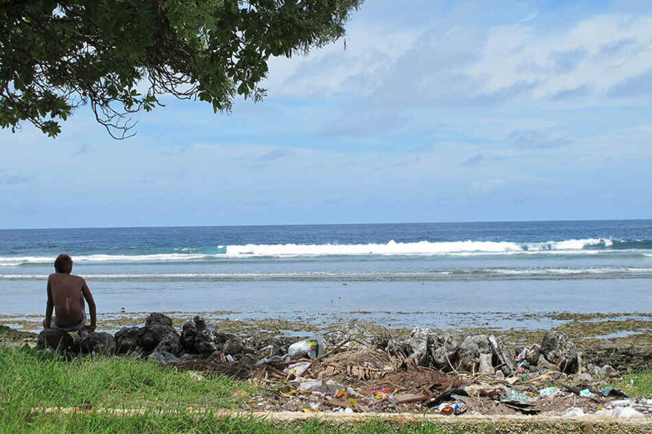 Ein Junge sitzt auf dem Atoll Tarawa am Sandstrand neben Abfällen.