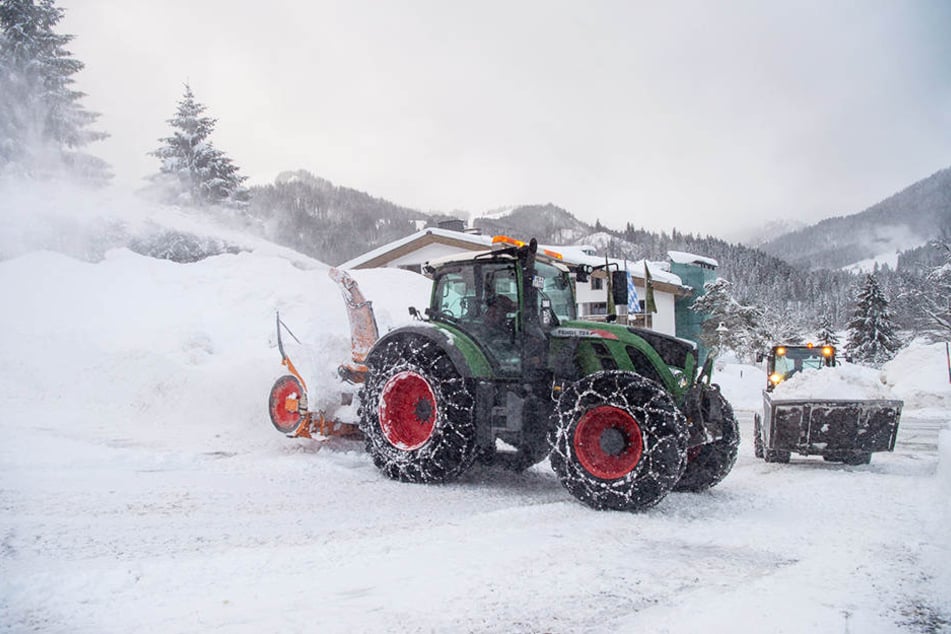 Eine Schneefräse und ein Radlader räumen einen zugeschneiten Parkplatz.