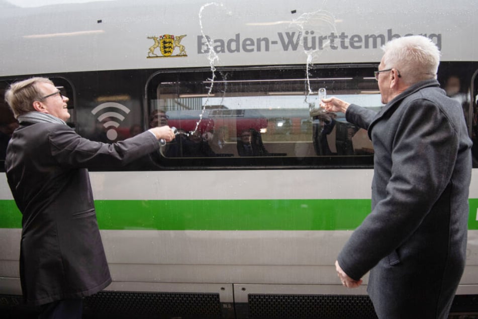 Winfried Kretschmann (rechts im Bild) und Ronald Pofalla schütten Sekt auf einen ICE 4.