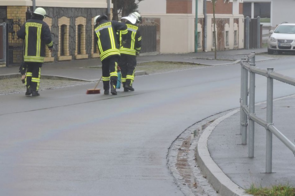 Kameraden säubern eine Straße im Muldental. Möglicherweise hatte ein defekter Bus hier große Mengen Diesel verloren.