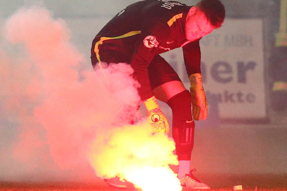 Fans vom FC Hansa Rostock zündeten Bengalische Feuer - Hansa-Keeper Marcel Schuhen versucht, ein brennendes Bengalo vom Rasen zu entsorgen.