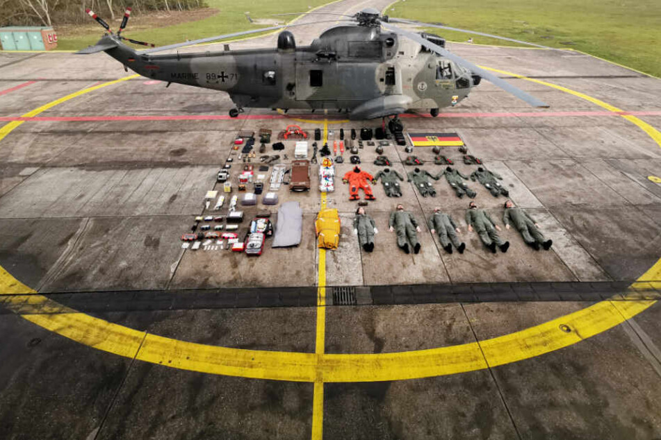 Stillgelegen! Fünf Seenotretter samt Ausrüstung liegen neben einem Rettungshelikopter SeaKing MK41.