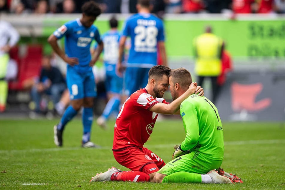 Düsseldorfs Niko Gießelmann (l) und Torwart Michael Rensing jubeln über ihren ersten Saisonsieg, während die Hoffenheimer Reiss Nelson (l.) und Adam Szalai (hinten, Nr. 28) mit hängenden Köpfen den Platz verlassen.