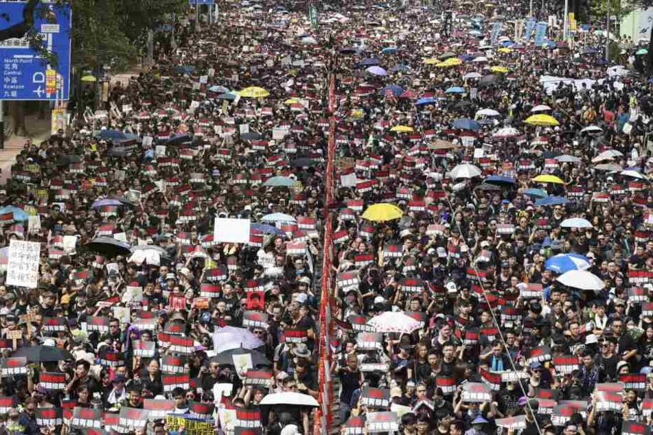 Menschen mit Regenschirmen und Protestschildern sind in Hongkong auf den Straßen.