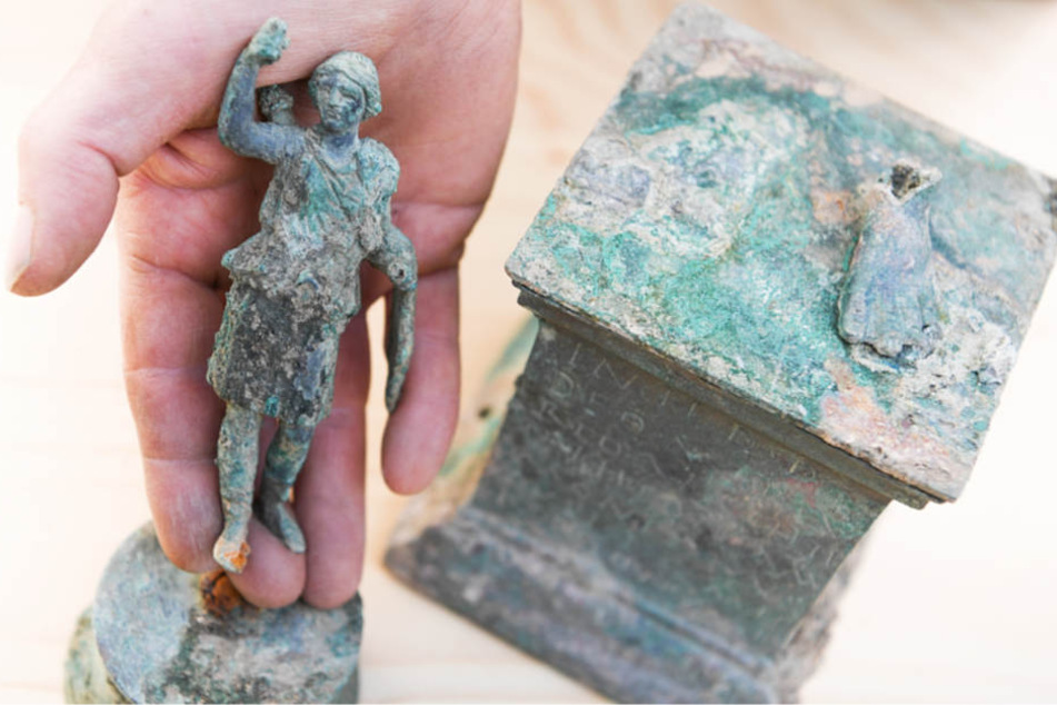 Ein Grabungstechniker präsentiert eine kleine Statue der Göttin Diana sowie den Sockel, auf dem einst die Figur des Merkurs stand.