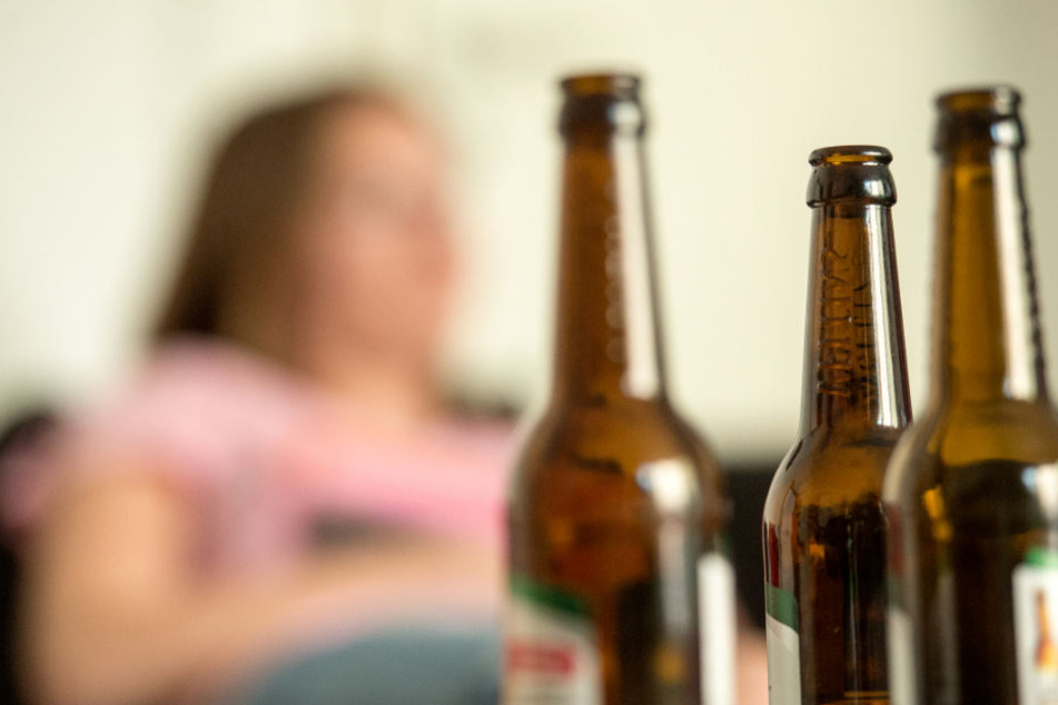 Eine junge Frau sitzt hinter leeren Bierflaschen. (Symbolbild)
