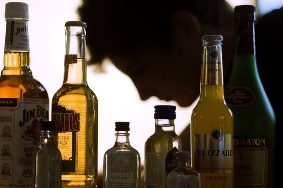 Ein Jugendlicher sitzt hinter mehreren Flaschen mit Alkohol.