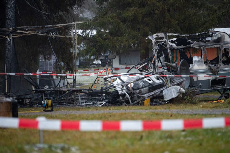 Die Reste des völlig abgebrannten Wohnwagen stehen auf einem Campingplatz.