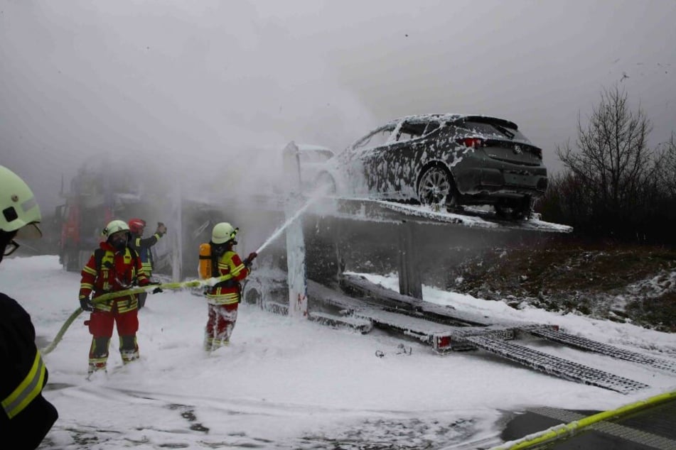Feuerwehrleute löschen den brennenden Autotransporter.