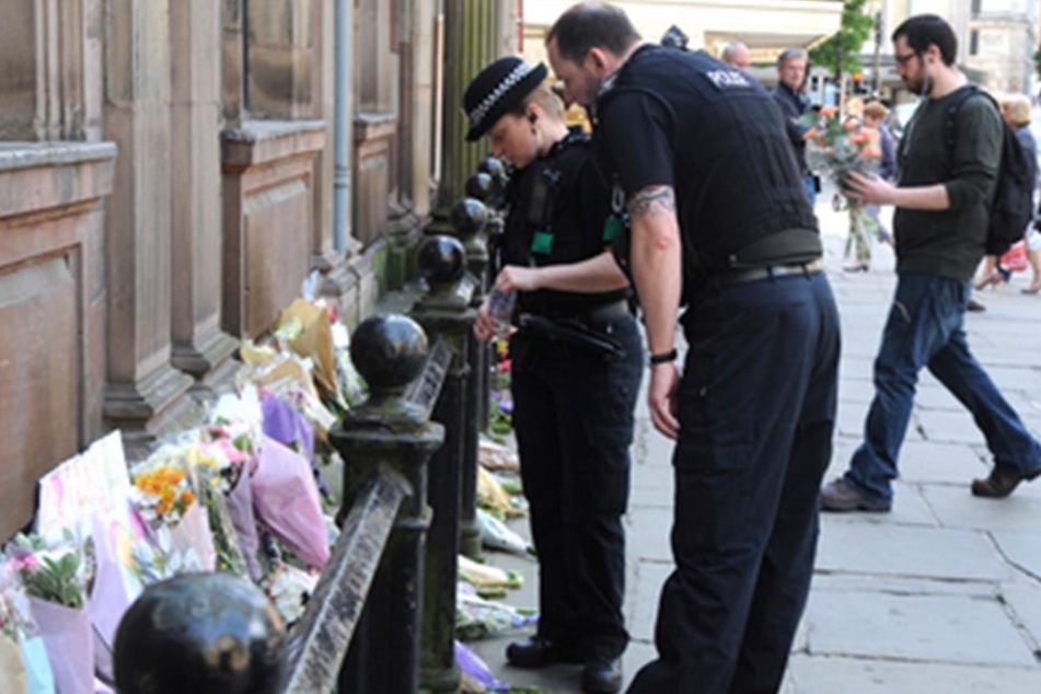 Britische Polizisten vor Blumensträußen und Beileidsbekundungen, die für die Opfer niedergelegt wurden.