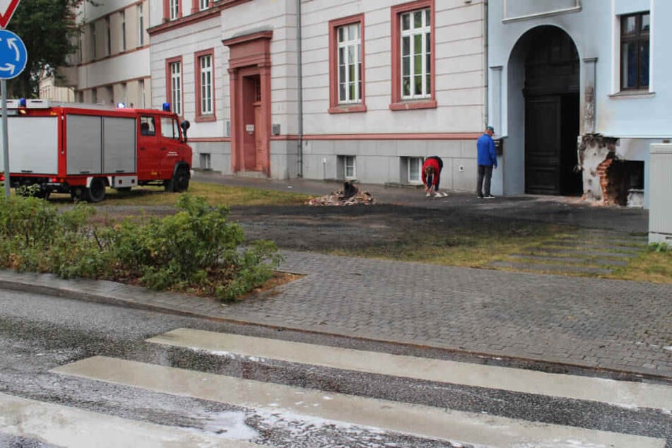 Ein Feuerwehrfahrzeug steht an der Unfallstelle an einem beschädigten Hauseingang.