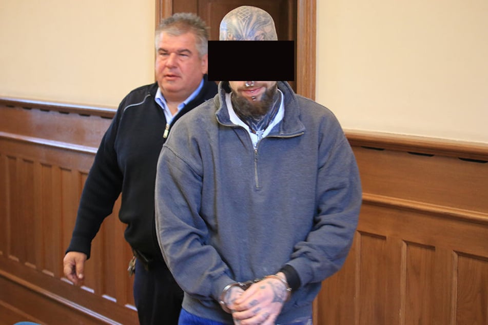 Ein Justizbeamter bringt einen der Angeklagten in Handschellen zum Prozess.
