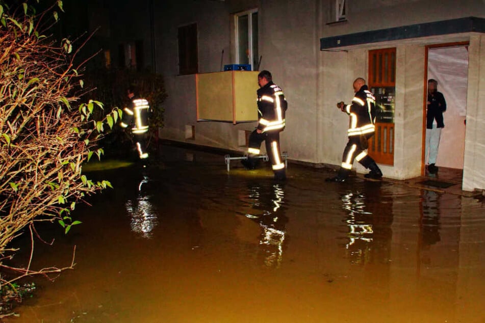 Feuerwehrleute laufen durch die Überschwemmung vor dem Mehrfamilienhaus.
