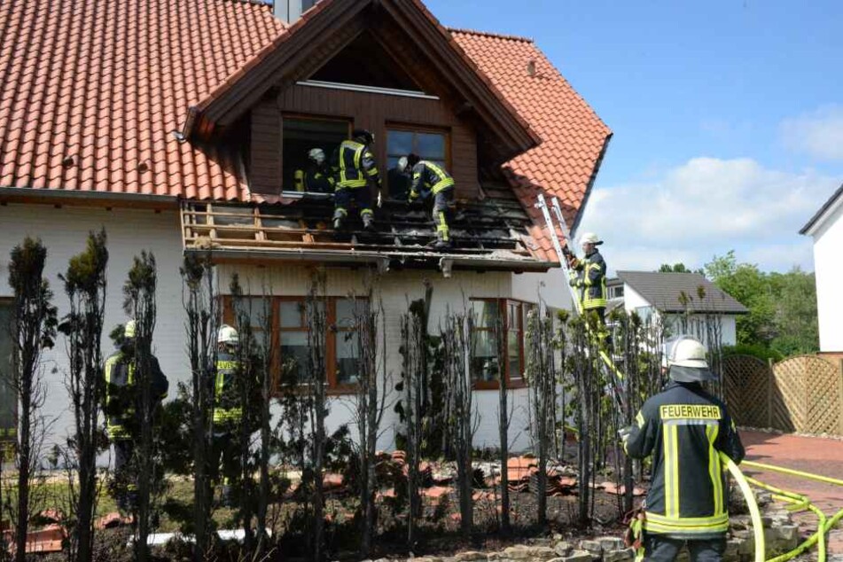 Hinter der völlig verkohlten Hecke löschen Feuerwehrleute Glutnester im Bereich des Daches.
