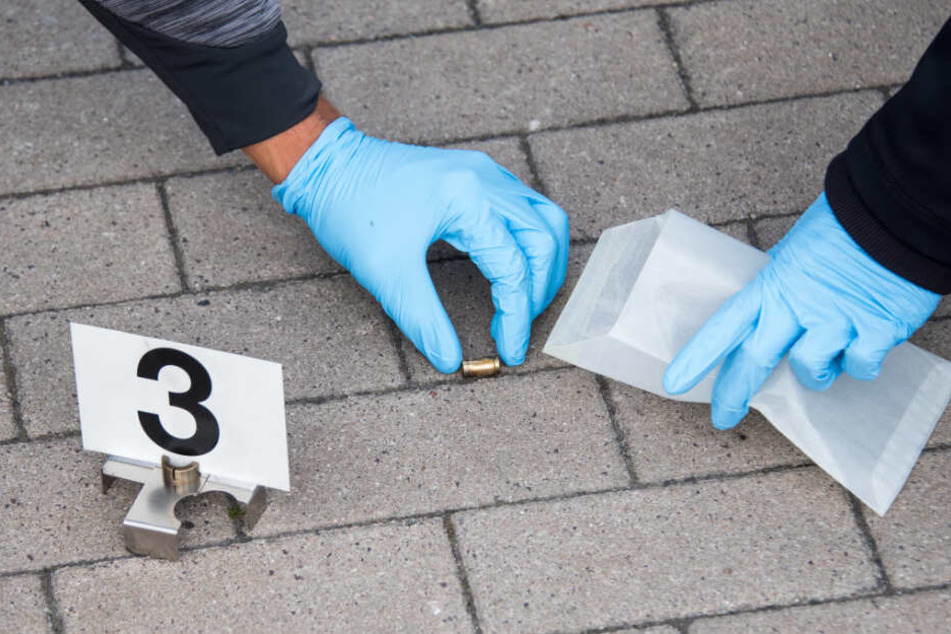 Einsatzbeamte heben die Patronenhülse auf und packen sie als Beweismittel in ein Päckchen.